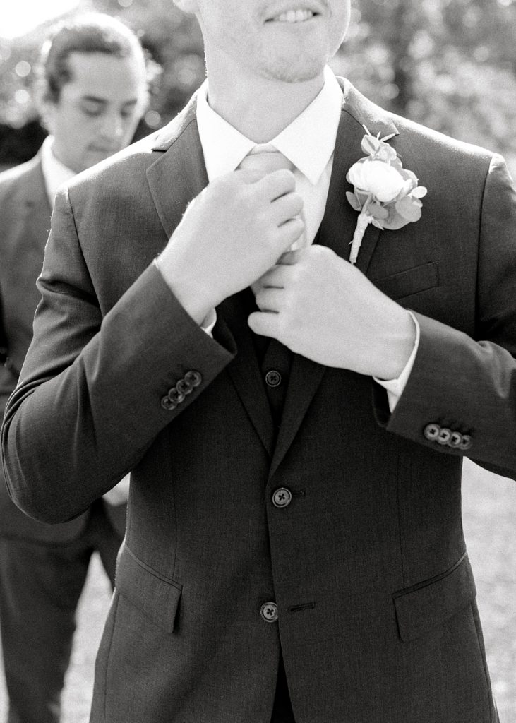 Detail photo of groom fixing tie.