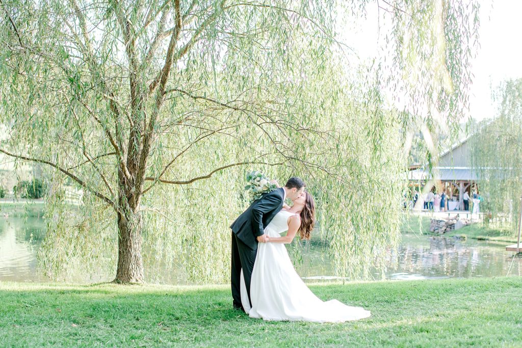 Bride and groom kiss under willow tree.