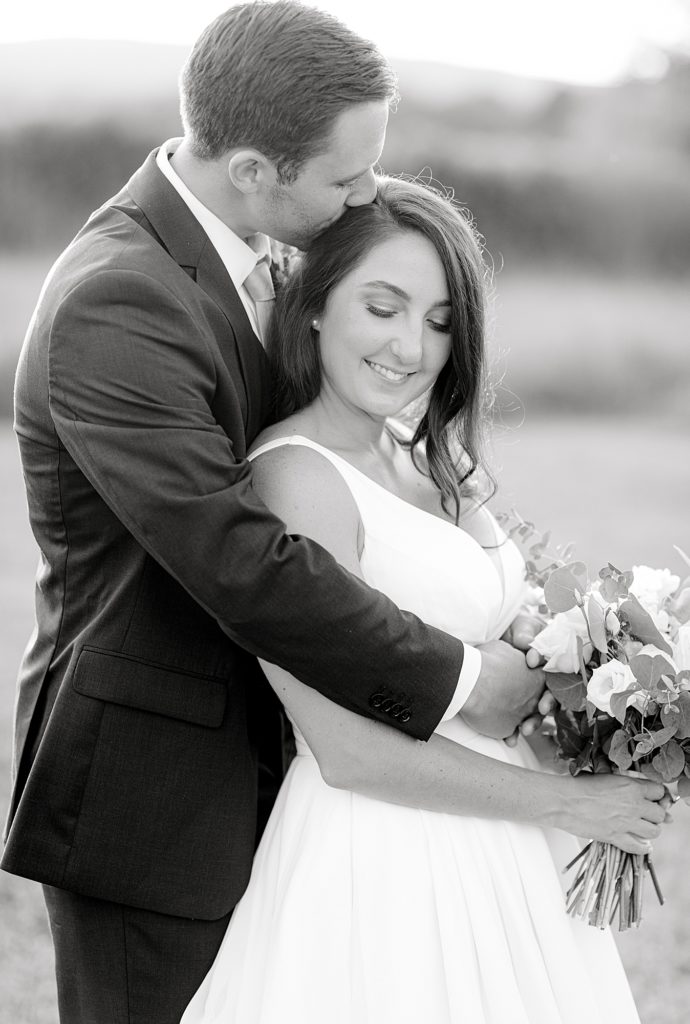 Black and white photo of groom kissing bride on forehead.