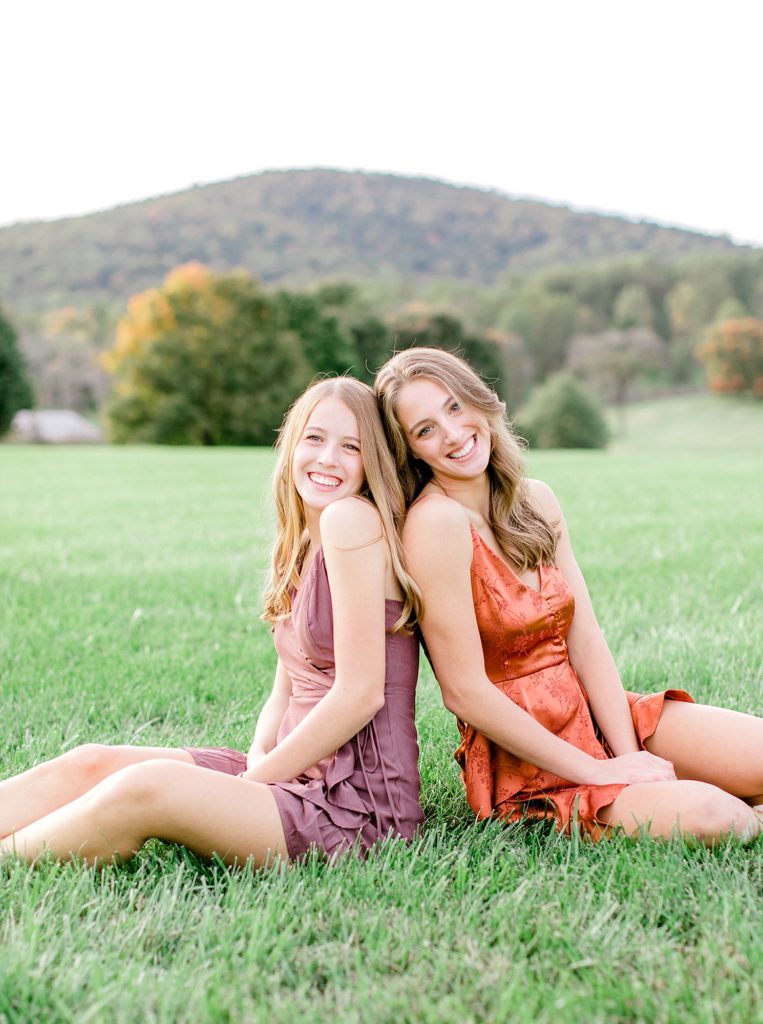 Sisters sitting in grass smiling for photo.