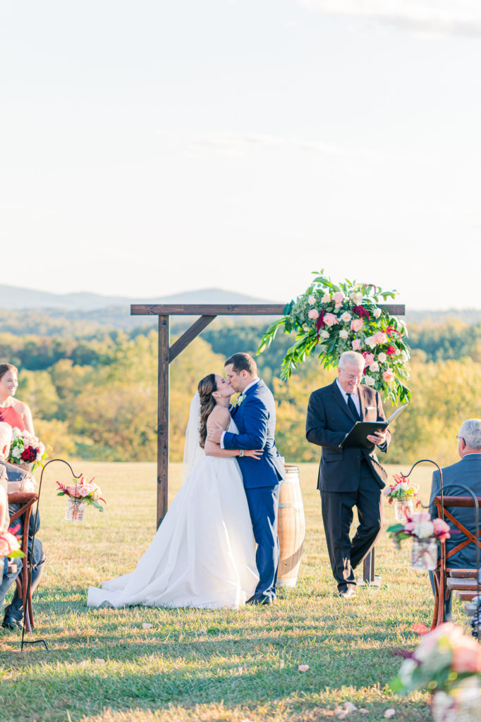 Bride and groom sharing first kiss and rose arch at wedding ceremony at Stone Tower Winery wedding.