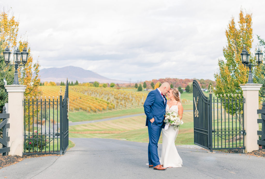 Wine country wedding in Harrisonburg, Virginia. Bride holding white and blue bouquet leaning in to kiss her groom in a blue tux at CrossKeys Vineyard.