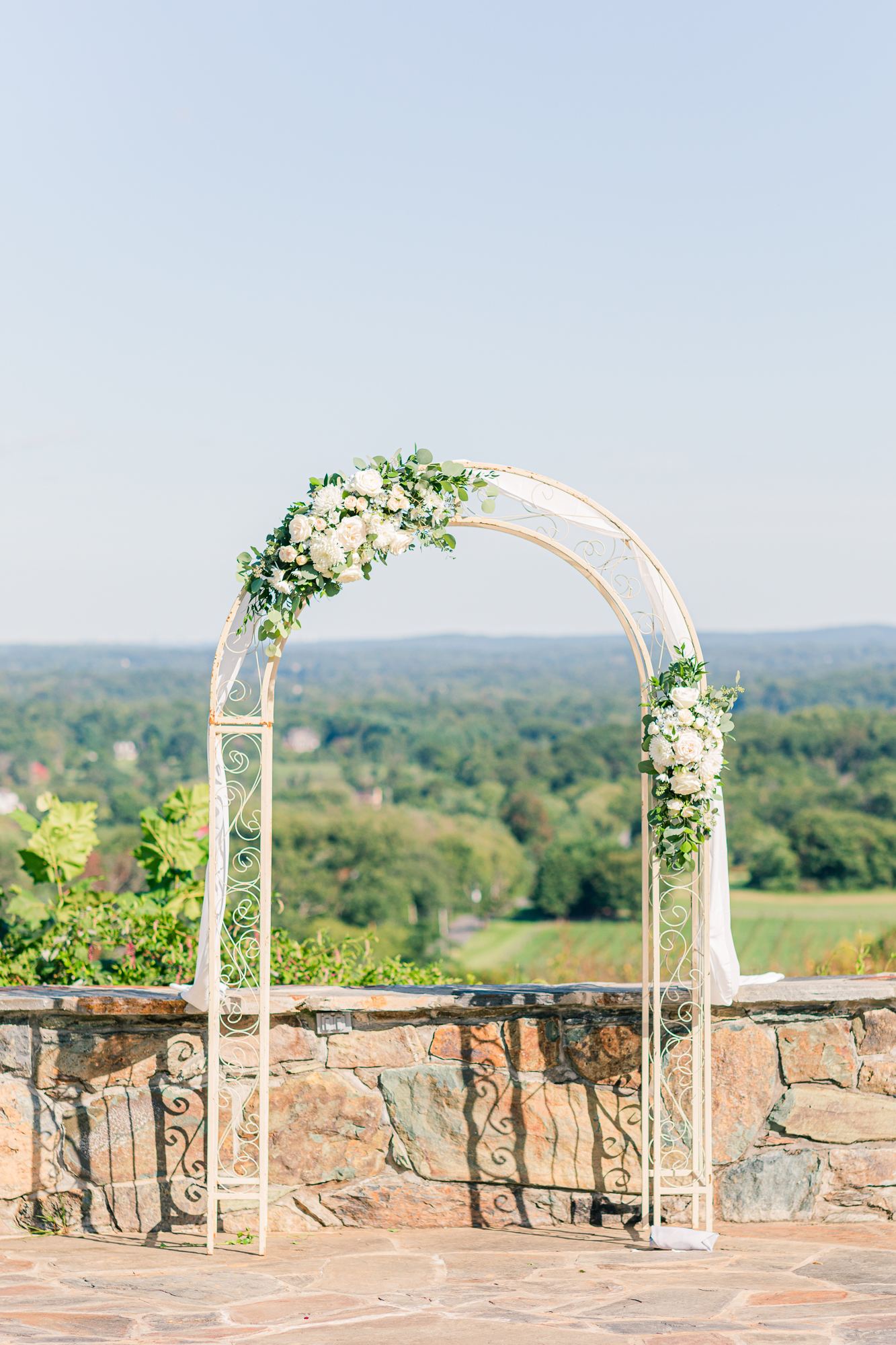 White metal arbor with white roses decorated for wedding ceremony at Bluemont Vineyards.