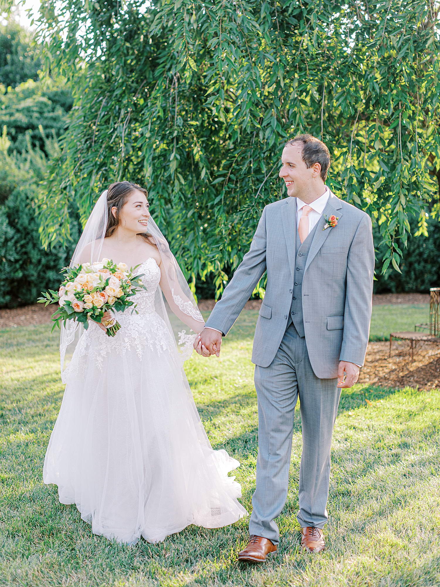 Bride holding coral and light pink bouquet walking with groom in grey tux and pink tie.