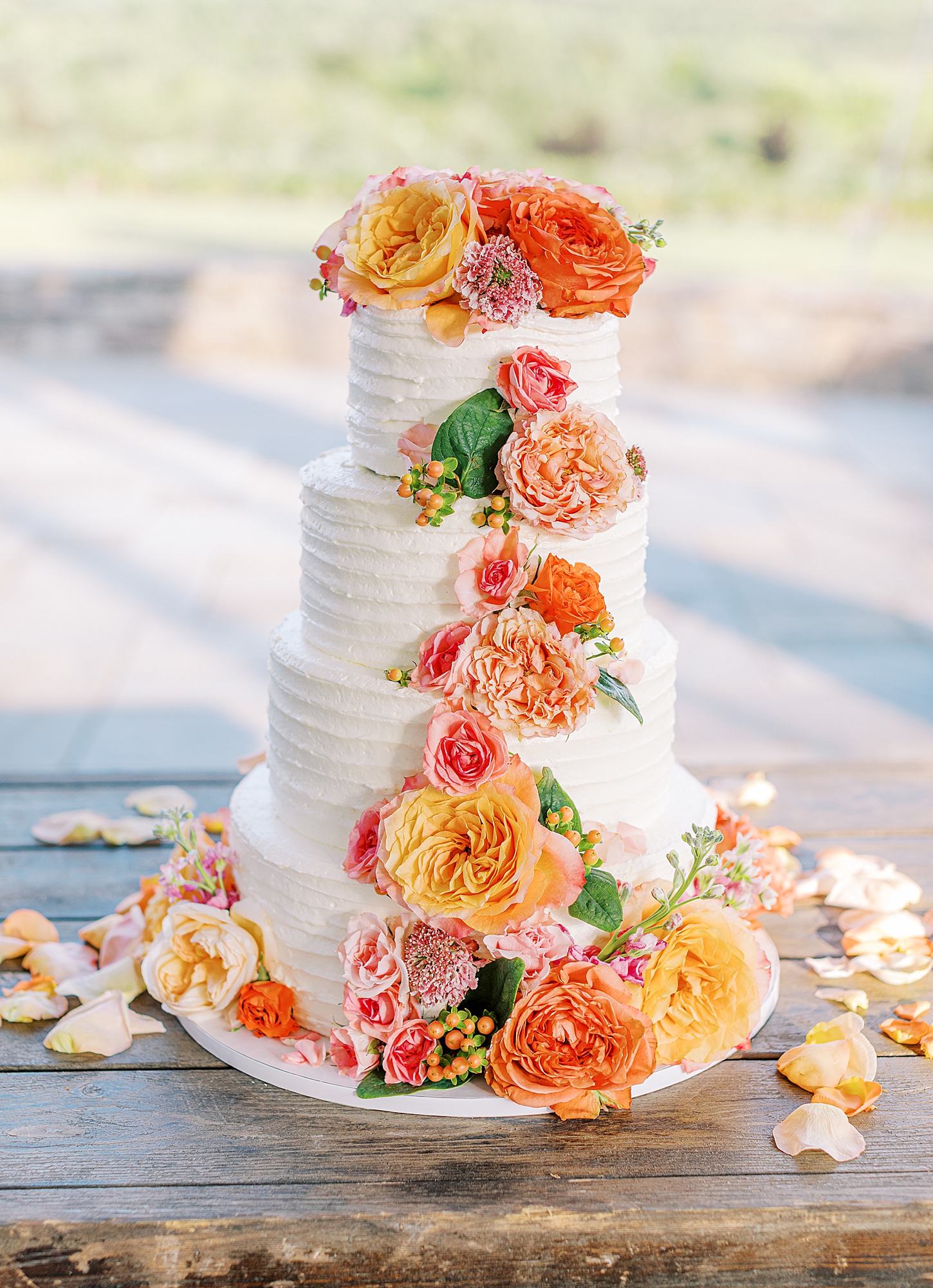 A four tiered wedding cake with pink and coral flowers.