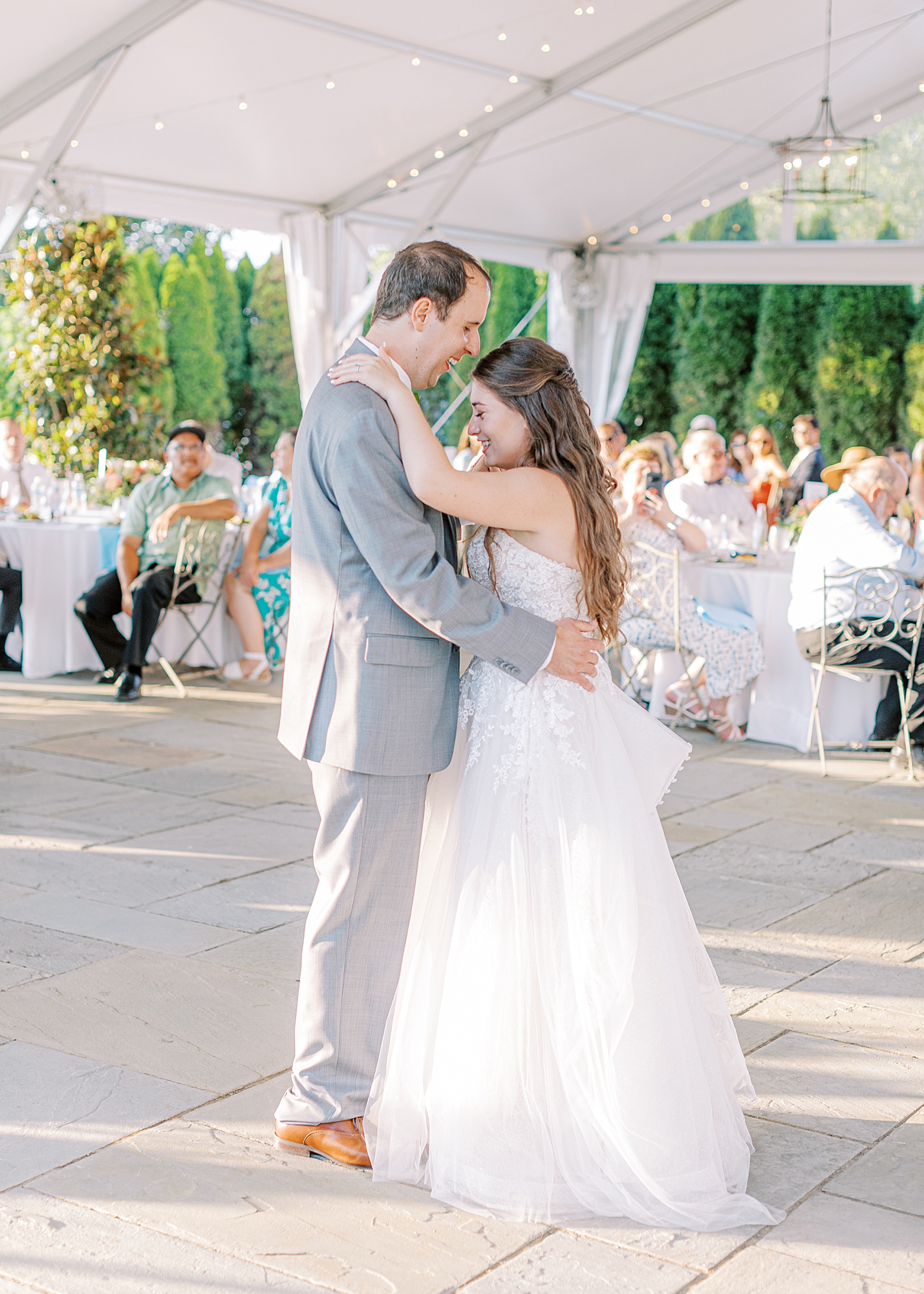 First dance between bride and groom in open aired luxury tent surrounded by hedges.