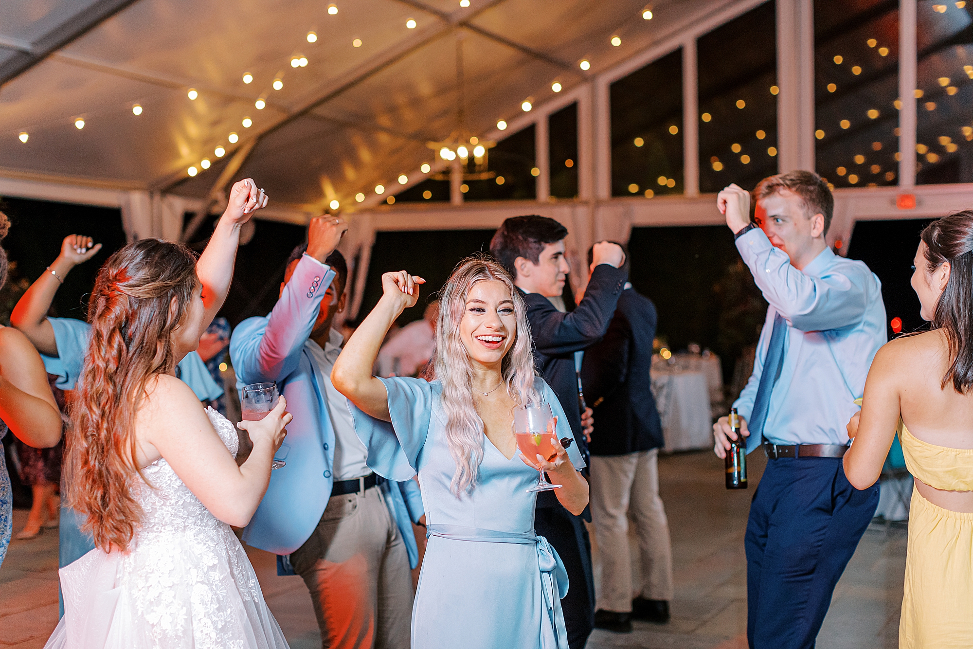 Bridesmaid dancing with drink in hand at reception under tent.