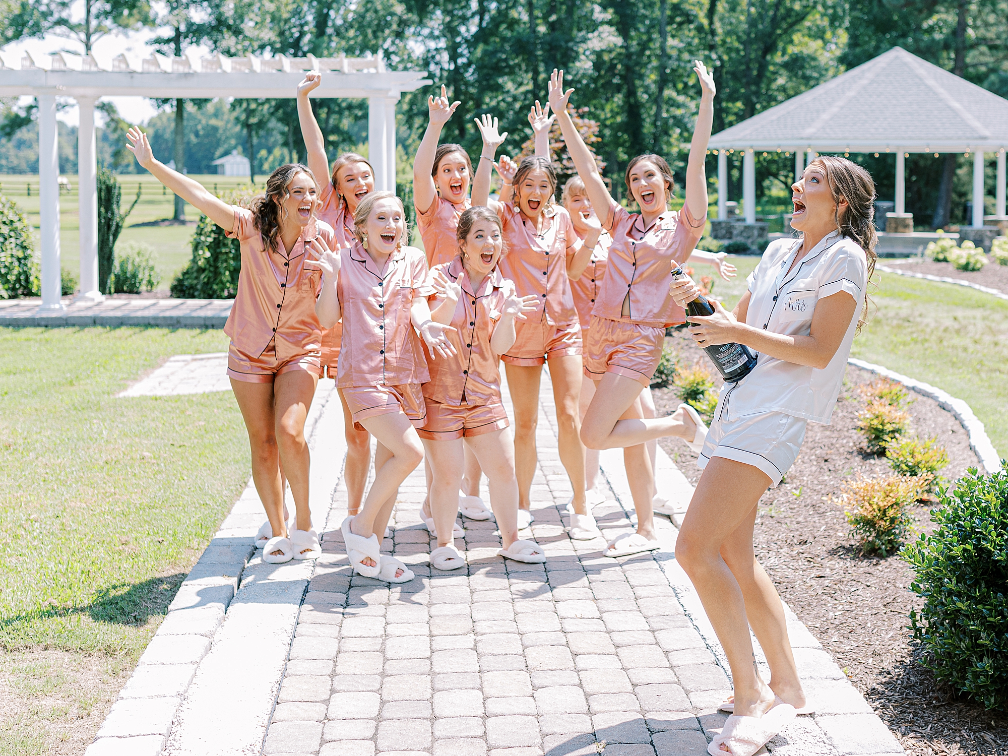 Bride popping champagne with bridesmaids in cute rose colored pajama set.
