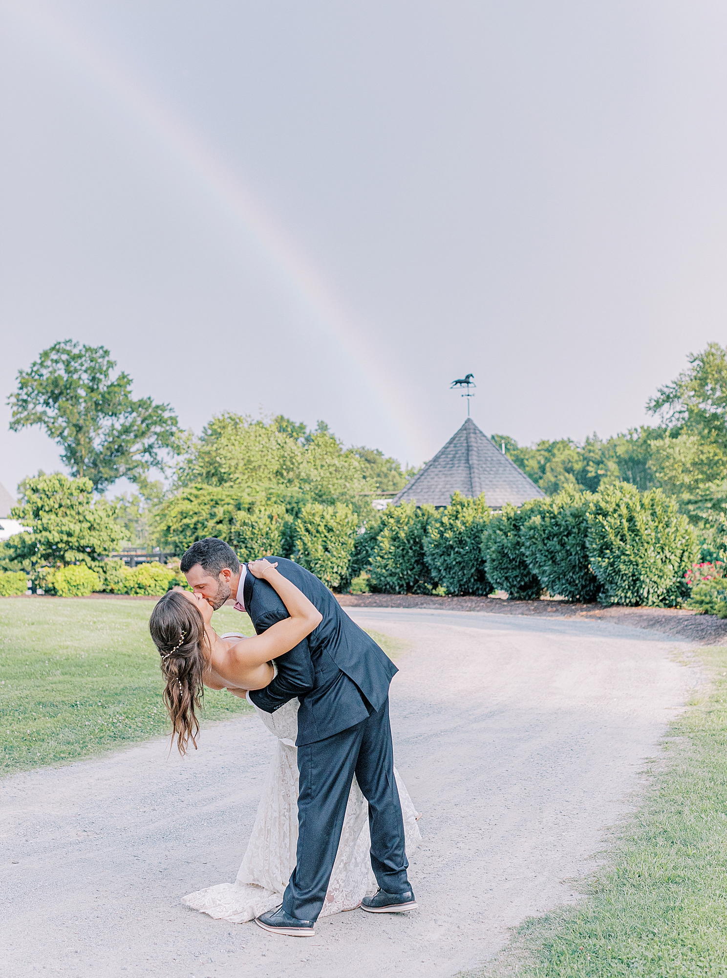 Rainbow behind bride and groom. Bride and groom kiss under rainbow.