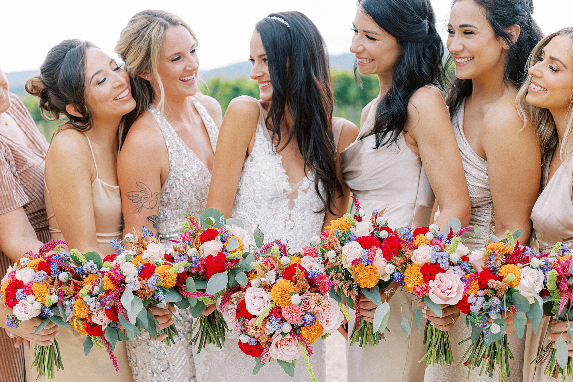 Bridesmaids in champagne colored dresses holding red and orange bouquets at Keswick Vineyards.