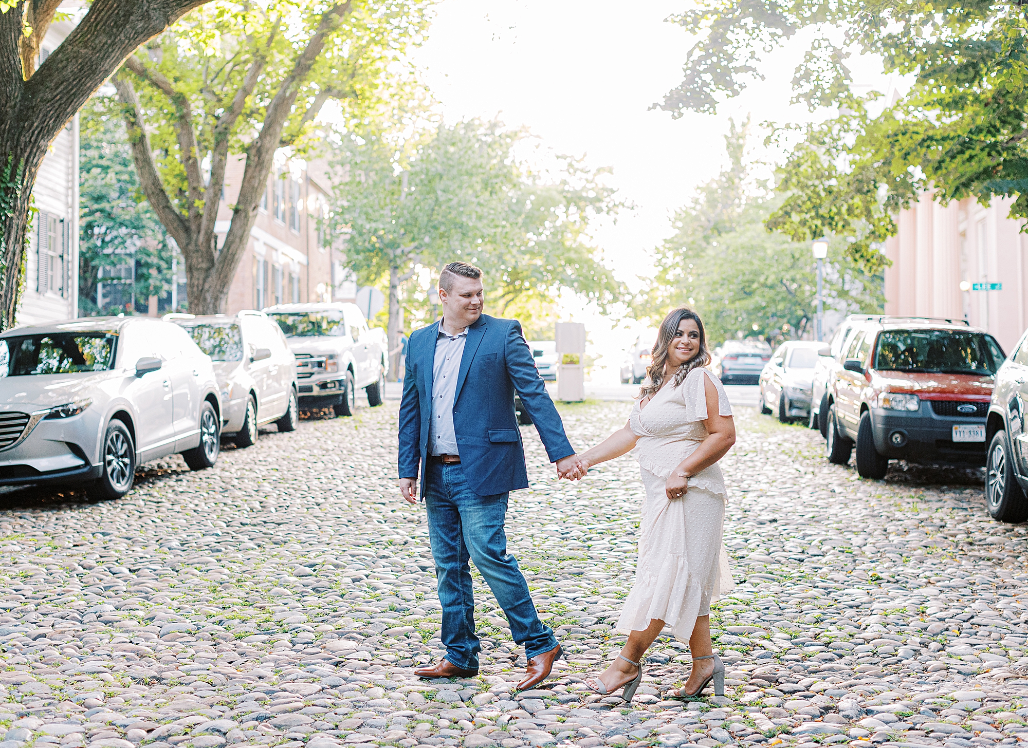 Portrait of man leading fiancée down the cobblestone streets of Old Town Alexandria during engagement session.