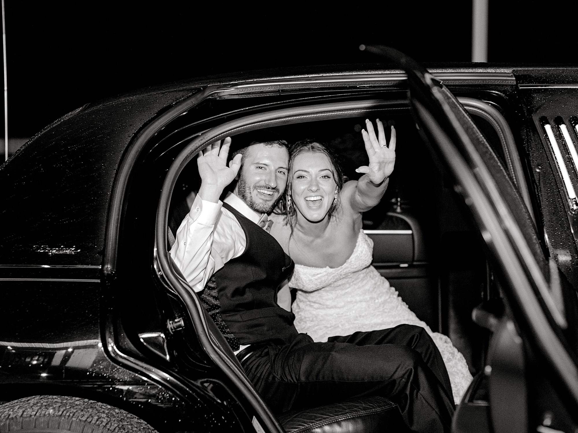 Bride and groom waving goodbye in limo.