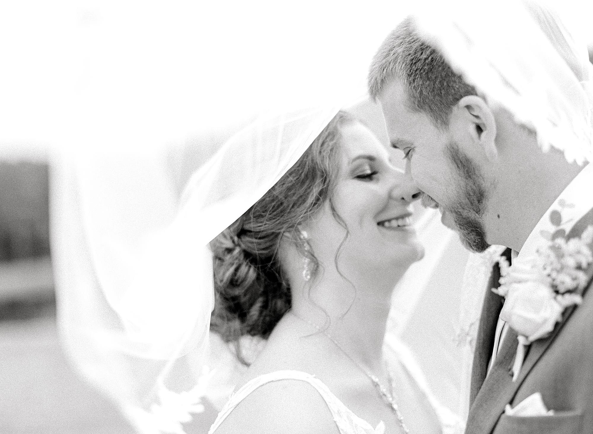 Black and white photo of bride and groom under veil.