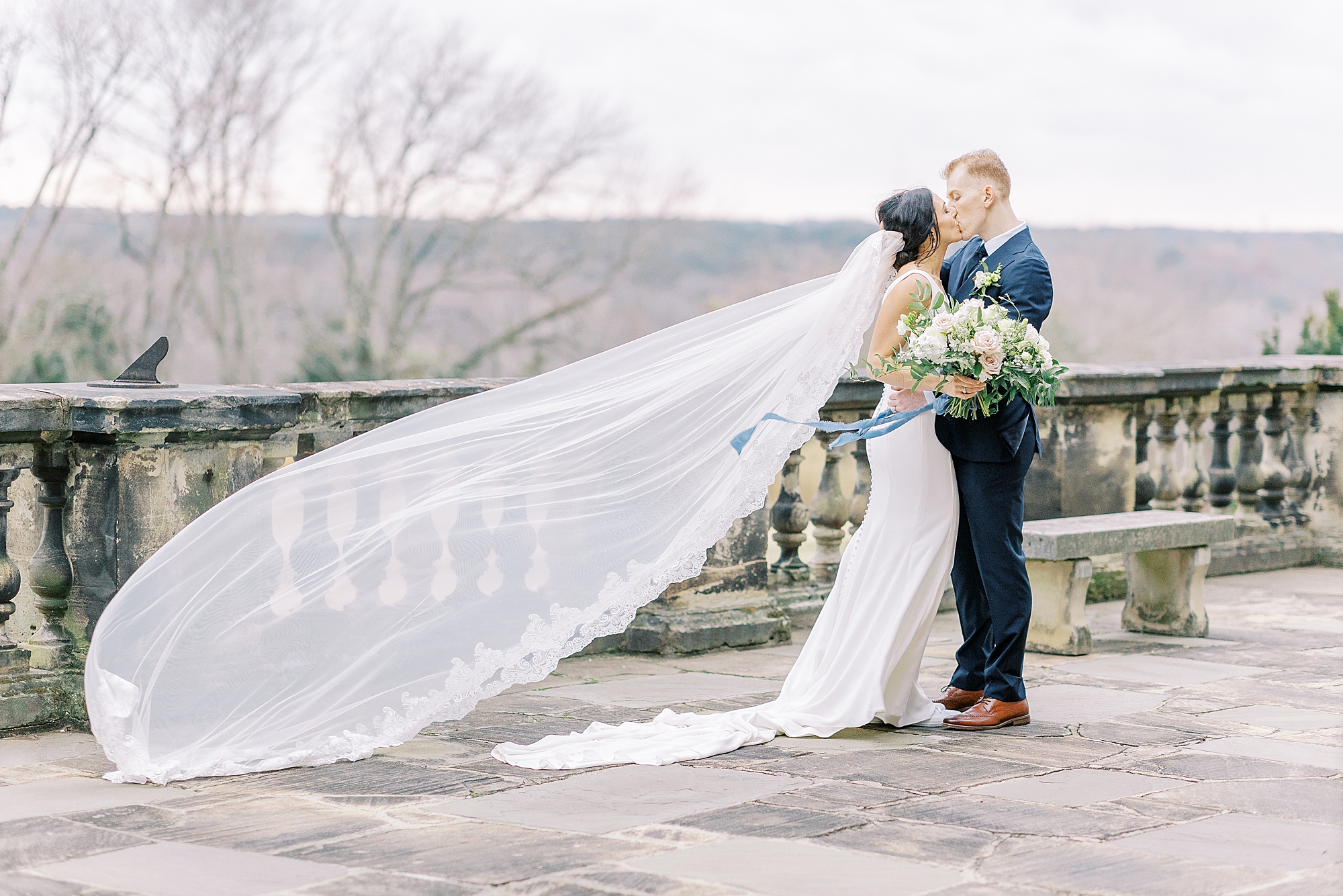 Richmond wedding photographer takes photo of veil flying in wind as bride kisses groom.