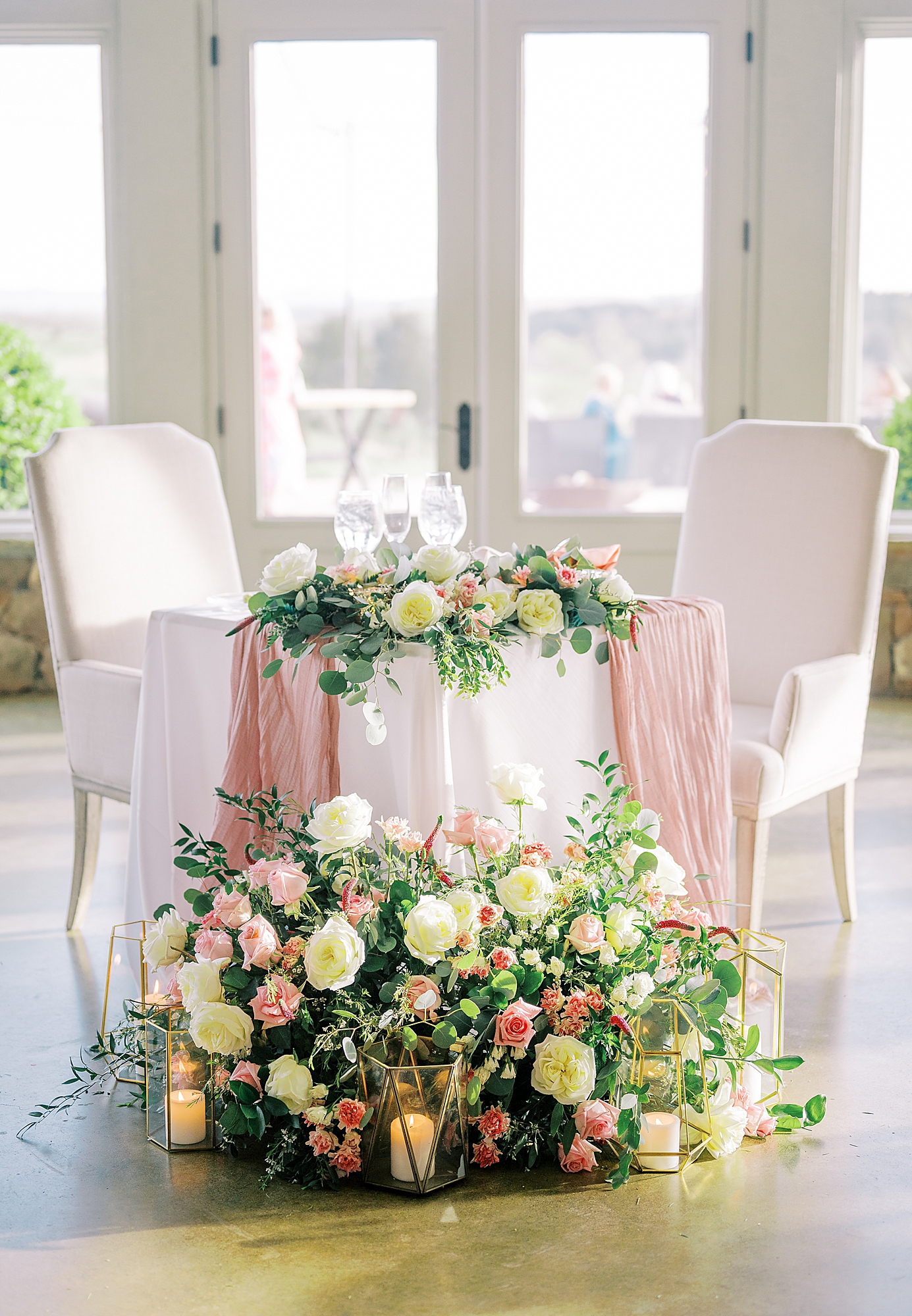 Sweetheart table covered in roses and greenery in ballroom at Stone Tower Winery.