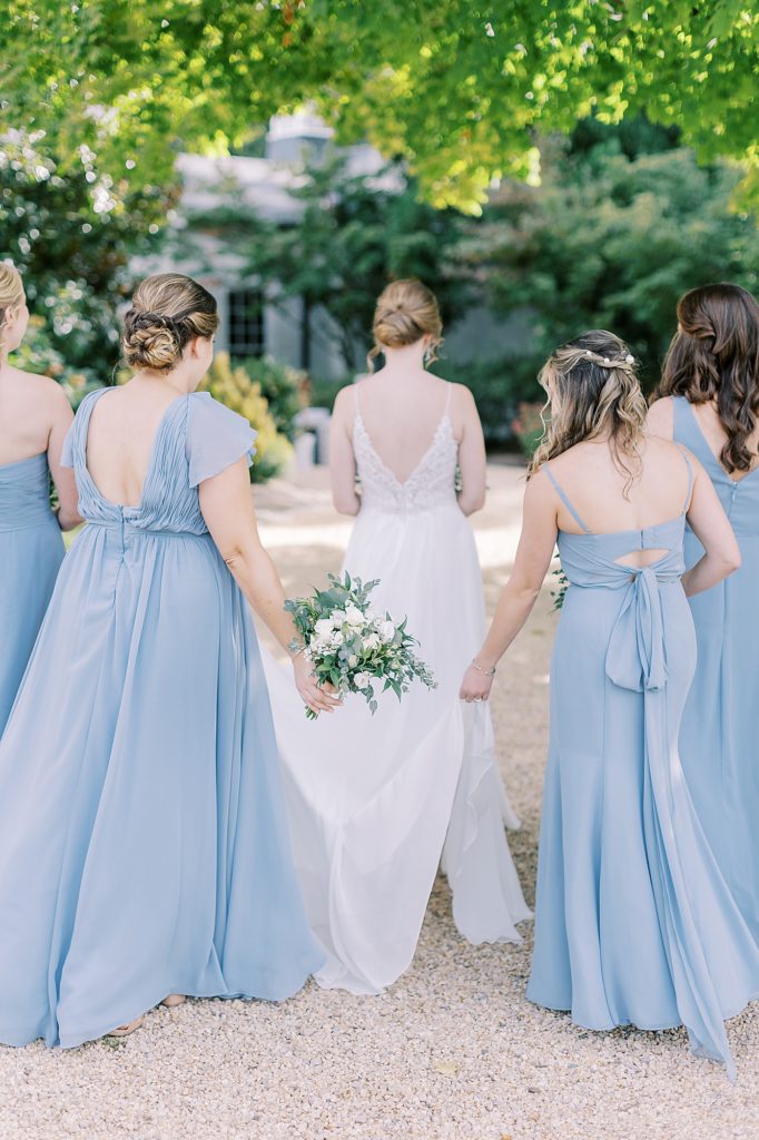 Fine art candid of bridesmaids helping carry bride's dress.