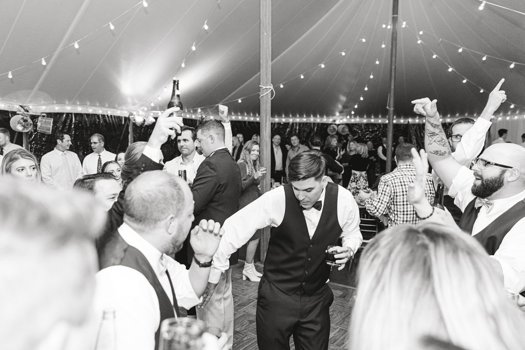 Black and white photo of groom dancing during tented reception.