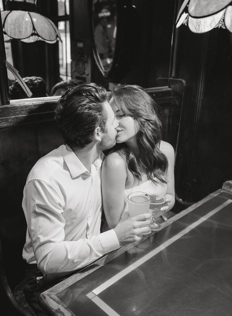 Bar engagement photo with couple sitting in booth kissing.