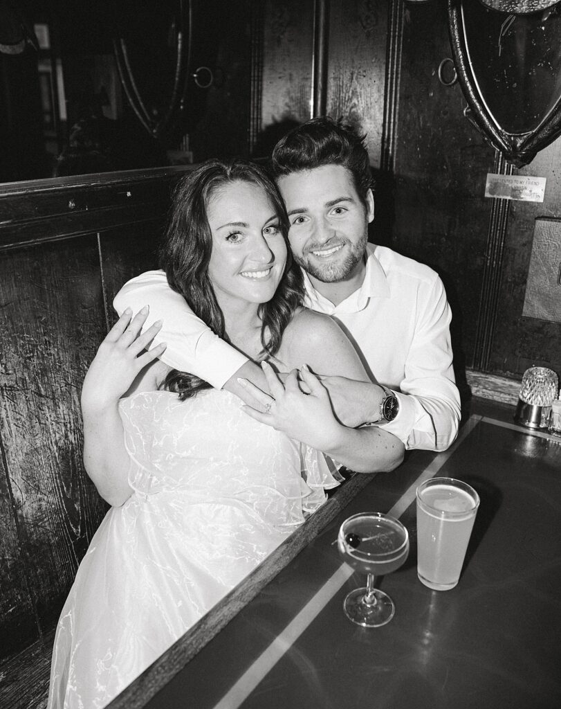Engagement photo in bar with couple sitting in booth smiling at camera.