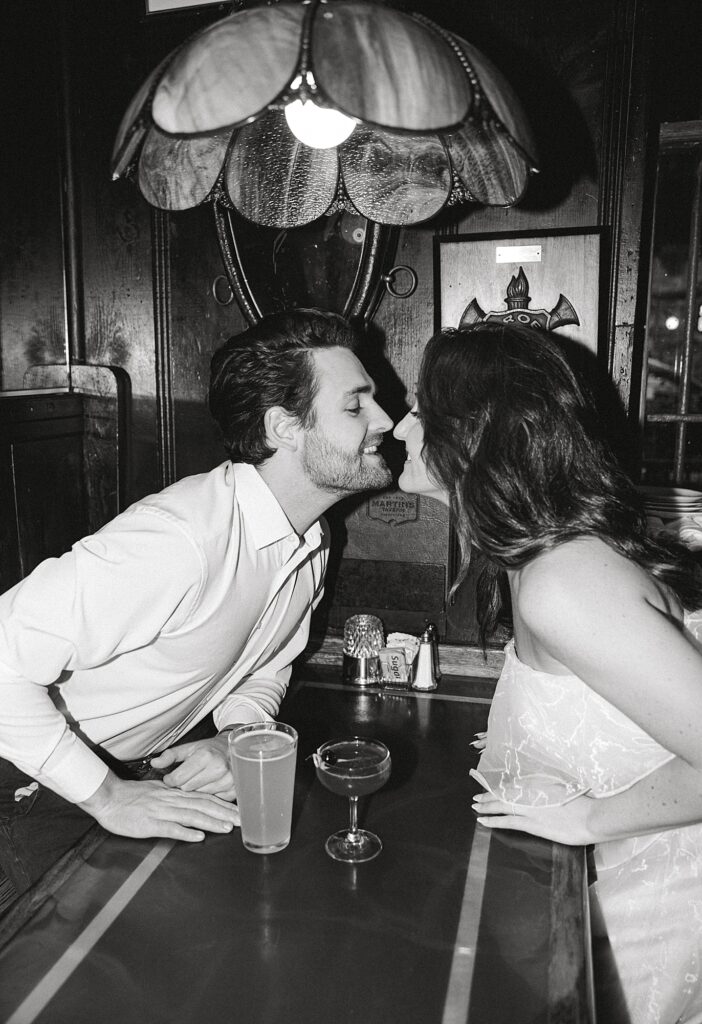 Vintage bar engagement photo with couple kissing across both.