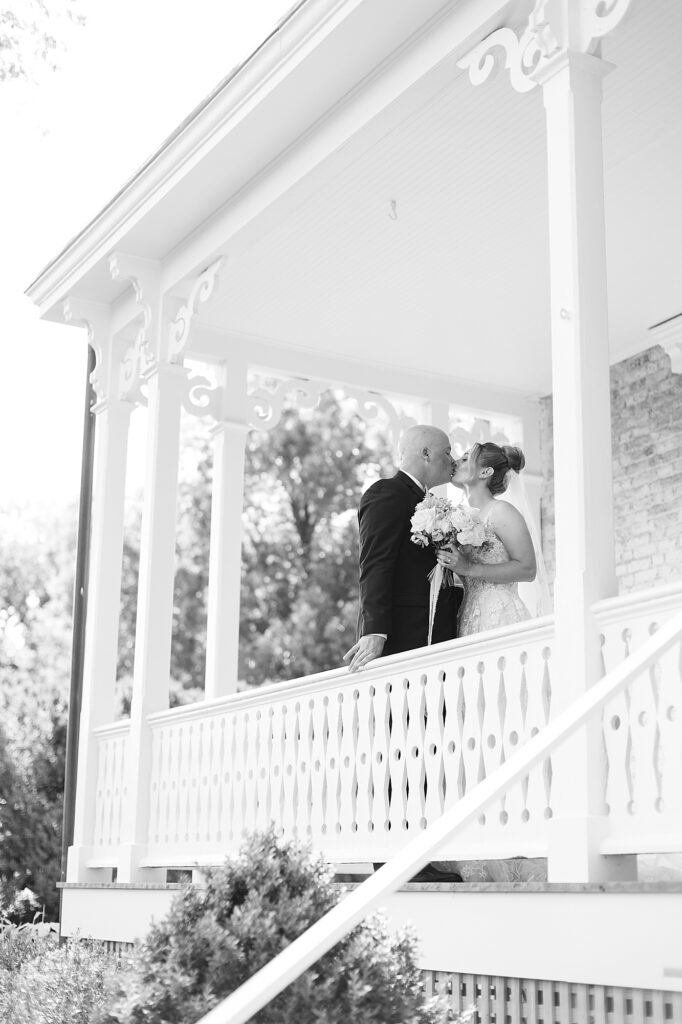Bride and groom kissing on porch of Boxwood Villa.
